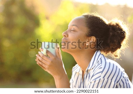 Profile of a relaxed black woman drinking coffee and smelling aroma in a park Royalty-Free Stock Photo #2290022151