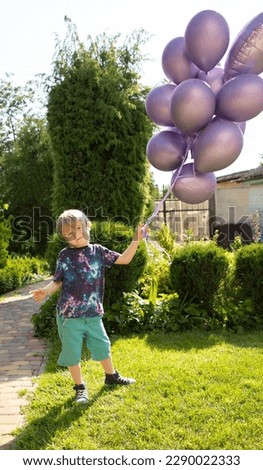 boy holds bunch of purple balloons with helium in summer in garden on sunny day. concept of joy, positivity and congratulations. festive mood, surprise. Family holidays, happy childhood, birthday