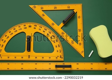 Protractor, triangle, ruler and sponge on green chalkboard, flat lay