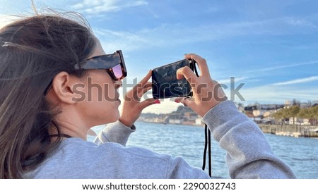 A tourist girl photographing a lake with her cell phone. View of a tourist girl taking photos with her cell phone