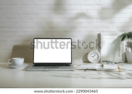 Front view of laptop with empty display, picture frame, coffee cup and notebook on white table.