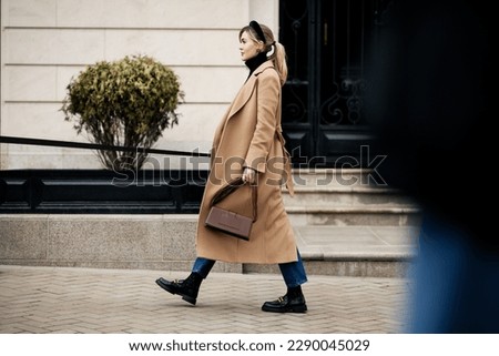Side view beautiful woman walking street in fashionable spring or autumn clothes cashmere coat, jeans, loafers shoes and small bag. Full length Female model in motion, street style fashion Royalty-Free Stock Photo #2290045029
