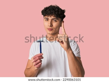 A young latin man holding a razor for shave showing number one with finger.