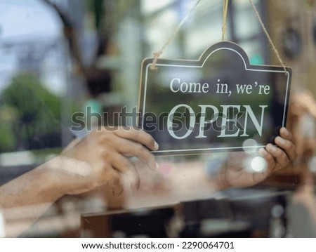 Shopkeeper setting open sign at coffeeshop for welcome the customer in coffee shop. Waiter in medical mask hanging card with open lettering on cafe entrance door. Small business and startup concept. Royalty-Free Stock Photo #2290064701