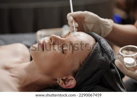 Esthetician applying glycolic acid peel on face of young woman Royalty-Free Stock Photo #2290067459