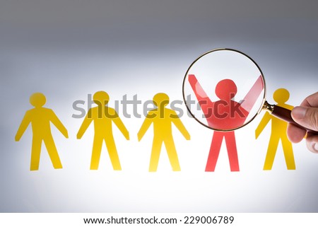 Cropped image of hand magnifying red paperman representing recruitment against gray background