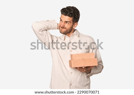 Young man holding a takeaway boxes isolated touching back of head, thinking and making a choice.