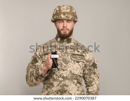 Soldier in military uniform holding medical tourniquet on light grey background. Space for text