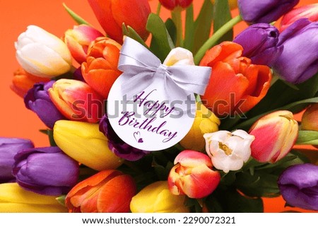 Beautiful bouquet of tulip flowers with Happy Birthday card on orange background, closeup