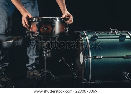 A male drummer and a drum kit on a black background, the musician is preparing to play.