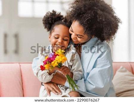Happy mother's day! Afro american family happy baby daughter congratulates mom on the holiday, hugs her and gives bouquet of flowers at home