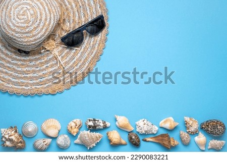Summer and vacation flat lay with woman straw hat, sun glasses and various seashells at the lower edge of the picture on blue background.