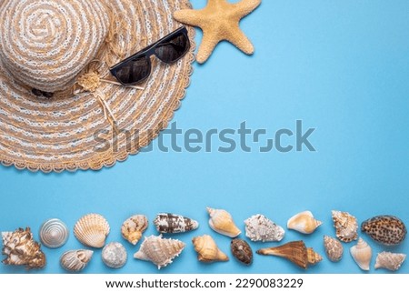 Summer and vacation flat lay with woman straw hat, sun glasses, a star fish and various seashells at the lower edge of the picture on blue background.