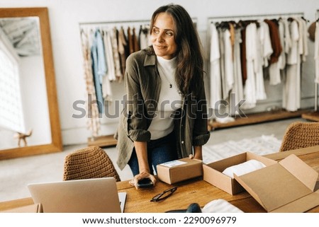 Driven by success and passion, this businesswoman prepares a shipping order in her boutique clothing store, determined to launch her online store and become a successful ecommerce entrepreneur. Royalty-Free Stock Photo #2290096979