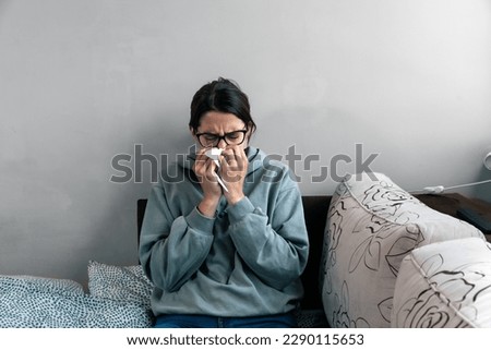Ill upset young woman sitting on sofa covered with blanket freezing blowing running nose got fever caught cold sneezing in tissue, sick girl having influenza symptoms coughing at home, flu concept Royalty-Free Stock Photo #2290115653