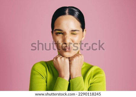 Latina woman wit flawless makeup winks at the camera in a studio. Wearing casual clothing, her beauty routine is highlighted with a graphic eyeshadow look, radiating her vibrant personality. Royalty-Free Stock Photo #2290118245