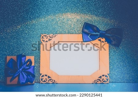 Mockup in a wooden horizontal frame decorated with a blue bow, next to a gift box. Template for greeting card on father's day