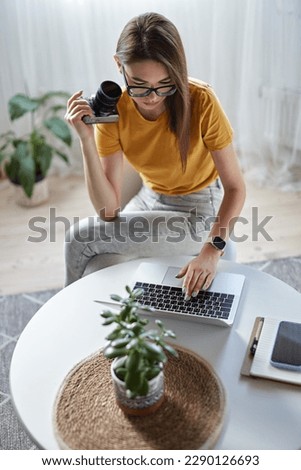 Young woman photographer working at home using computer sitting at table at home