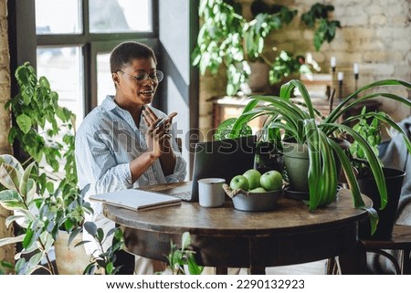 Young attractive African American woman nutritionist is working on laptop in a beautiful green space, home or modern office. Healthy food, apples, water. Video consultation, conference, presentation