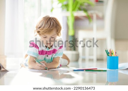 Child drawing lying on the floor. Kid painting rainbow. Online remote learning arts and crafts homework for school kids. Little boy with colorful pencils. Children draw. Creativity and imagination fun