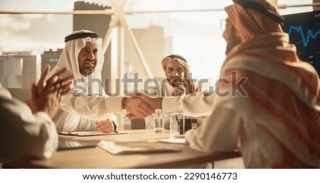 Middle Eastern Business Partners Striking a Successful Deal at a Corporate Modern Meeting Room. Two Arab Men Shaking Hands, Managers in Traditional White Robes Celebrating and Clapping Hands Royalty-Free Stock Photo #2290146773