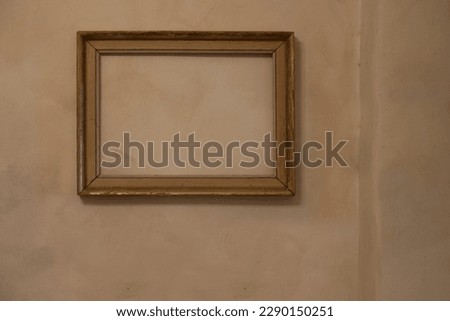 Empty frame with no painting in it hanging on a pale orange wall  with Venetian stucco. Art home interior concept with copy space.