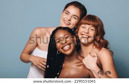 Cheerful women with different skin tones smiling at the camera in a studio. Group of happy young women embracing their natural skin. Portrait of three body positive young women standing together. Royalty-Free Stock Photo #2290151041