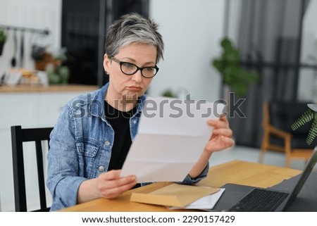 Upset senior woman reading mail or bill at table. Royalty-Free Stock Photo #2290157429