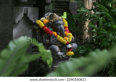 Traditional Ganesha statue with flower wreath in Balinese garden. Lord Ganesha is believed to bring good luck and thus he is worshipped before anything new is started. Royalty-Free Stock Photo #2290160811