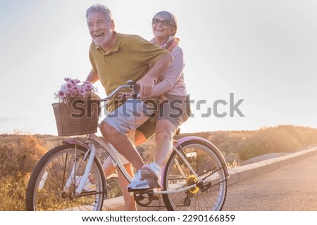 Youthful and playful happy senior old couple enjoy outdoor leisure activity riding together the same bike. Man carrying aged woman in healthy active lifestyle. Retired people using bicycle Royalty-Free Stock Photo #2290166859