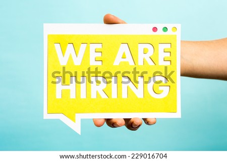 Hand holding we are hiring announcement with cutout letters paper on vibrant yellow speech bubble and all over blue background. Job concept. Royalty-Free Stock Photo #229016704