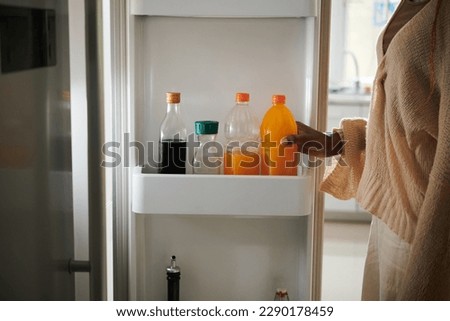 Woman taking bottle of orange soft drink from fridge Royalty-Free Stock Photo #2290178459