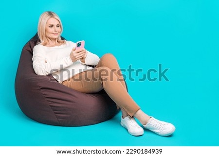 Full length photo of cute sweet lady dressed white shirt sitting bean bag texting device empty space isolated teal color background