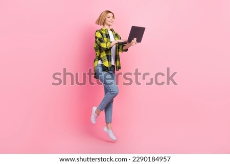Full length photo of charming sweet lady wear plaid shirt jumping high typing modern gadget isolated pink color background