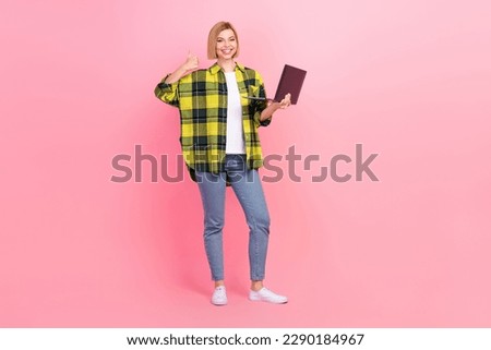 Full body photo of lovely young lady show thumb up hold gadget dressed stylish checkered yellow garment isolated on pink color background