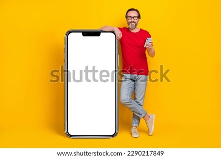 Photo of charming pretty guy pensioner dressed red t-shirt glasses typing gadget empty space isolated yellow color background
