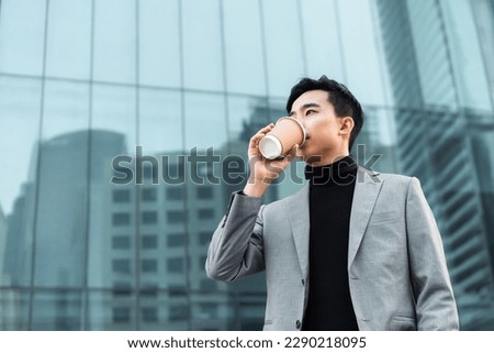 Asian businessman is drinking take away coffee outdoors in the city. 