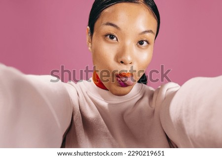 Gen Z woman taking a fun selfie while wearing bold lipstick in a studio. Young woman sticking her tongue out and looking at the camera as she takes a self-portrait. Royalty-Free Stock Photo #2290219651