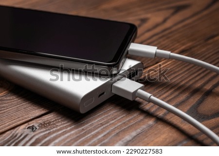 Powerbank and charge smartphone on wooden table.
