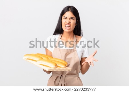 pretty hispanic chef woman looking angry, annoyed and frustrated and holding a tray with bread buns