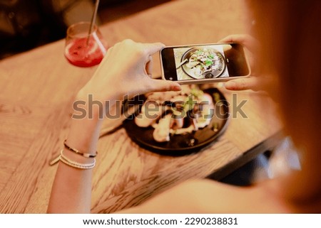 Blogger. Woman photographsplate with institution 's signature dish while sitting in restaurant. Enjoying taste. Recreation and entertainment. Delicious food. Specialty of establishment.