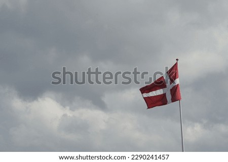 Red and white Denmark flag moving in the wind with cloudy grey sky in the background