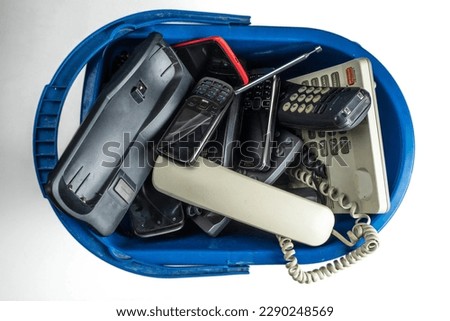 Old desk phones, cordless phone, cell phones, and smartphones in a trash can isolated on a white background. Royalty-Free Stock Photo #2290248569