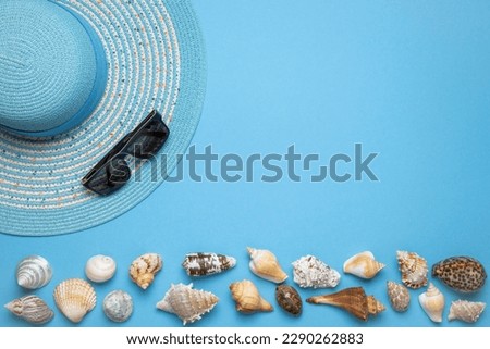 Summer and vacation flat lay with a beauty blue striped woman straw hat, sun glasses and various seashells at the lower edge of the picture on blue background.