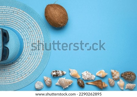 Summer and vacation flat lay with a beauty blue striped woman straw hat, sun glasses, a Coconut and various seashells at the lower edge of the picture on blue background.