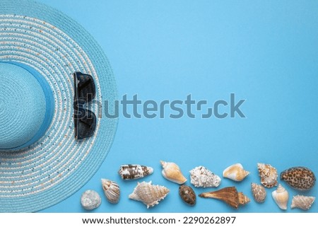 Summer and vacation flat lay with a beauty blue striped woman straw hat, sun glasses and various seashells at the lower edge of the picture on blue background.