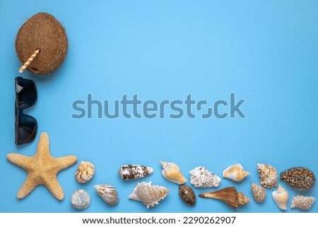 Summer and vacation flat lay with sun glasses, a Coconut with straw, a big star fish and various seashells at the lower edge of the picture on blue background.