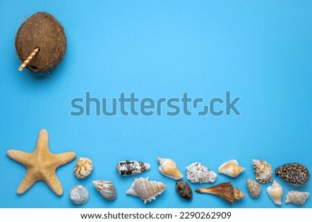 Summer and vacation flat lay with a Coconut with straw, a big star fish and various seashells at the lower edge of the picture on blue background.