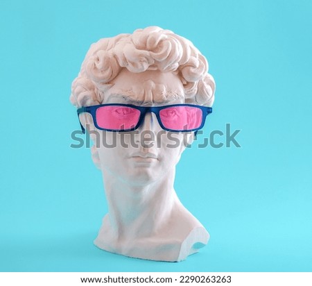 Plaster statue head wearing blue glasses on blue background.