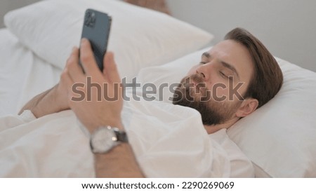 Young Adult Man using Phone while Lying in Bed